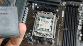 An image showing an AMD Ryzen 7 7800X3D CPU installed on a motherboard with a person in the foreground holding the socket cap in their hand.
