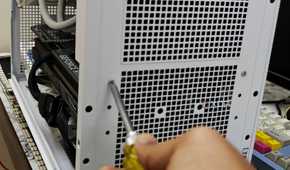 An image showing a person undoing the screws holding the PSU on the case.