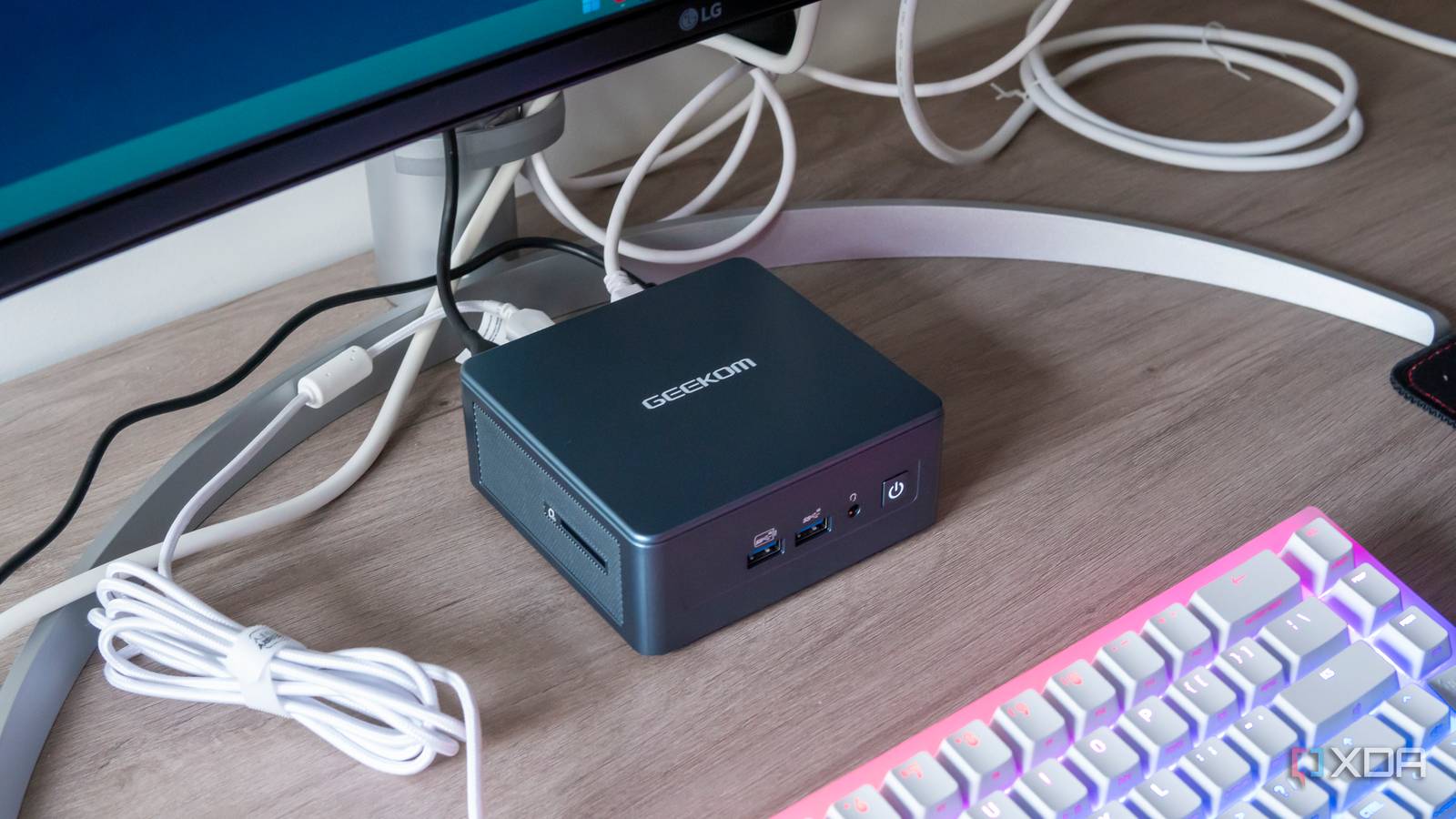 Geekom Mini IT13 mini PC under a monitor with a keyboard in front of it