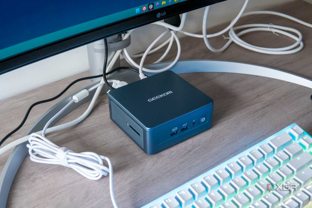 Geekom Mini IT13 mini PC under a monitor with a keyboard in front of it