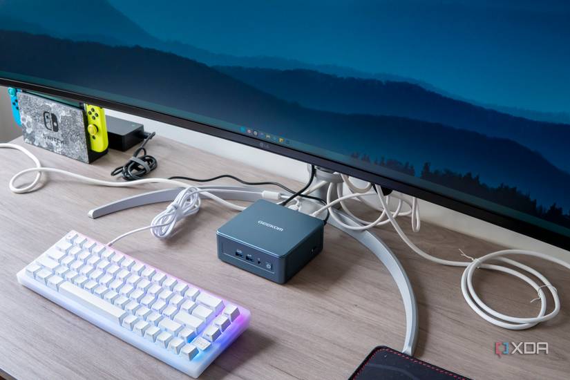 Angled view Geekom Mini IT13 mini PC under a monitor with a keyboard in front of it