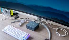 Angled view Geekom Mini IT13 mini PC under a monitor with a keyboard in front of it