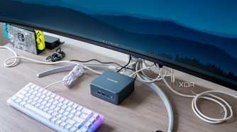 Angled view Geekom Mini IT13 mini PC under a monitor with a keyboard in front of it