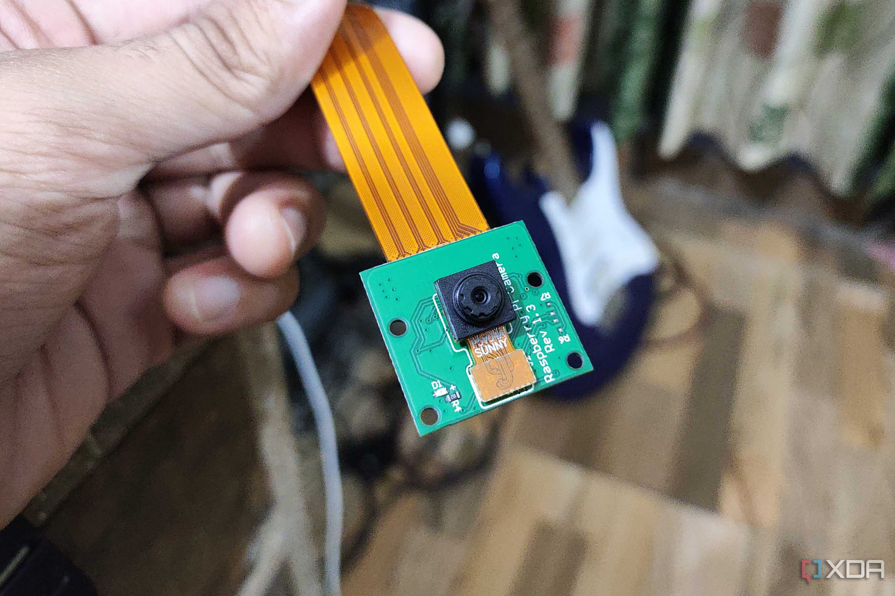 A person holding a Raspberry Pi Camera rev 1.3, with a guitar in the background