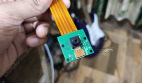 A person holding a Raspberry Pi Camera rev 1.3, with a guitar in the background