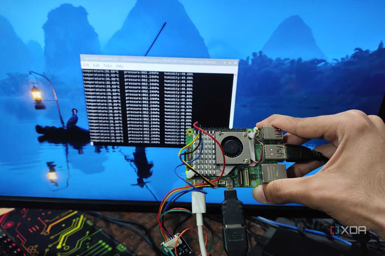 A person holding a Raspberry Pi 5 with a BME280 sensor attached to it in front of a screen