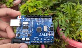 An Arduino board held in front of some plants
