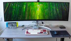 A desk setup with multiple devices, including a Geekom A8 PC under a large ultrawide monitor