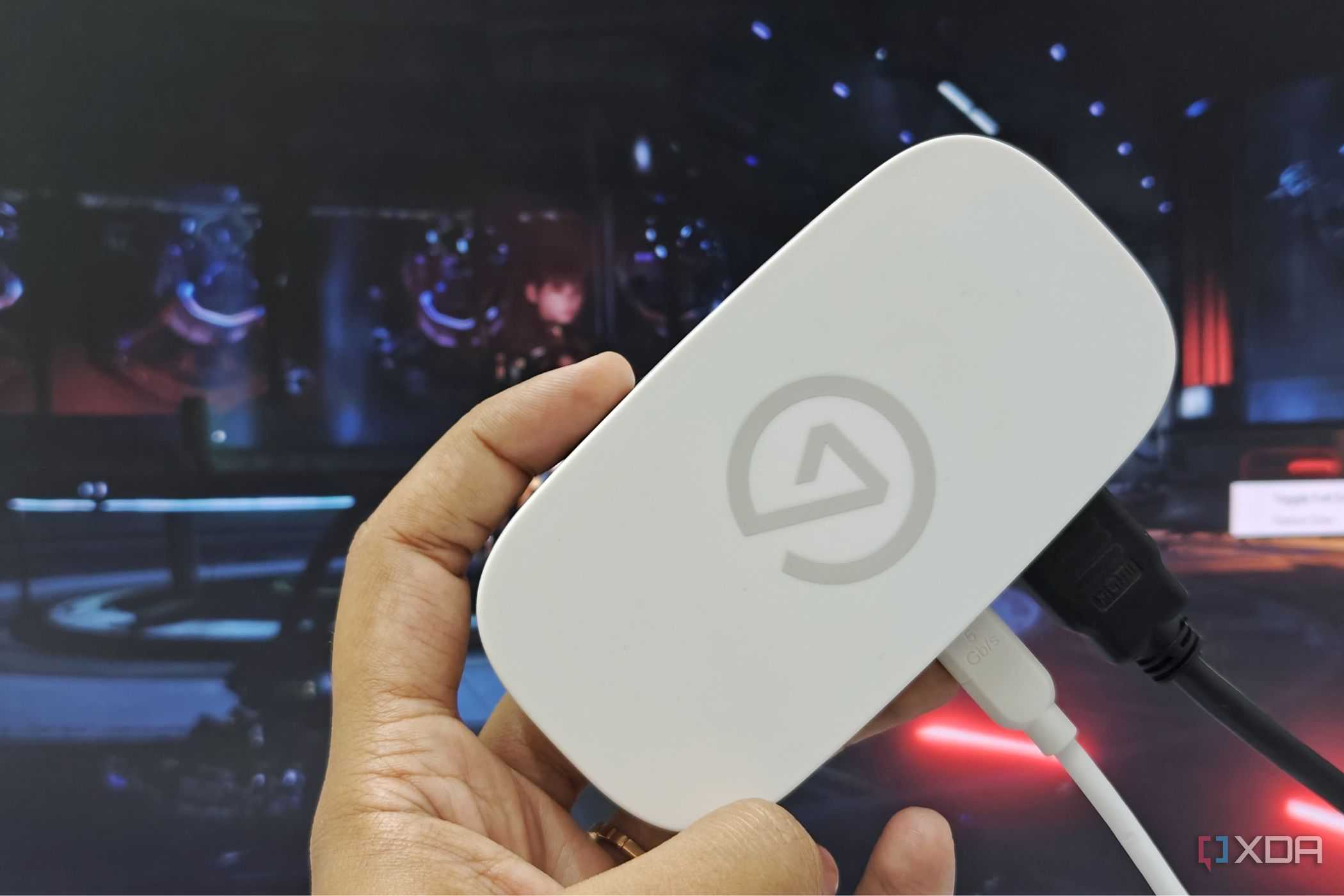 An image showing a person holding an Elgato Game Capture Neo in front of a monitor.