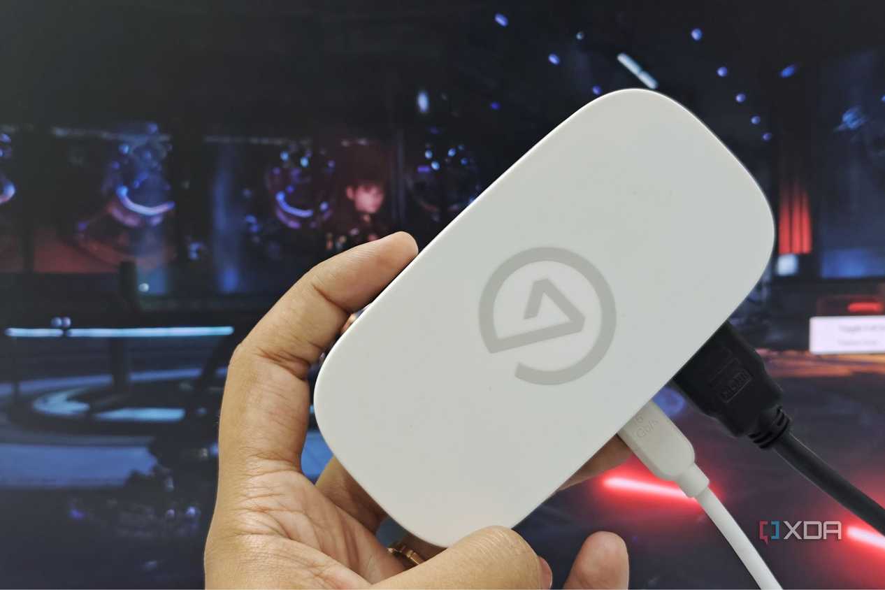 An image showing a person holding an Elgato Game Capture Neo in front of a monitor.
