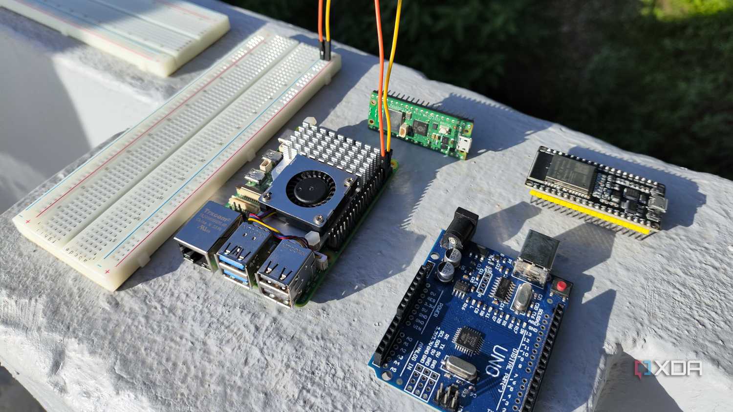 A breadboard connected to a Raspberry Pi 5, with microcontrollers lying around them