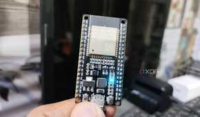 A person holding an ESP32, with an LED glowing on the microcontroller