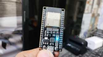 A person holding an ESP32, with an LED glowing on the microcontroller
