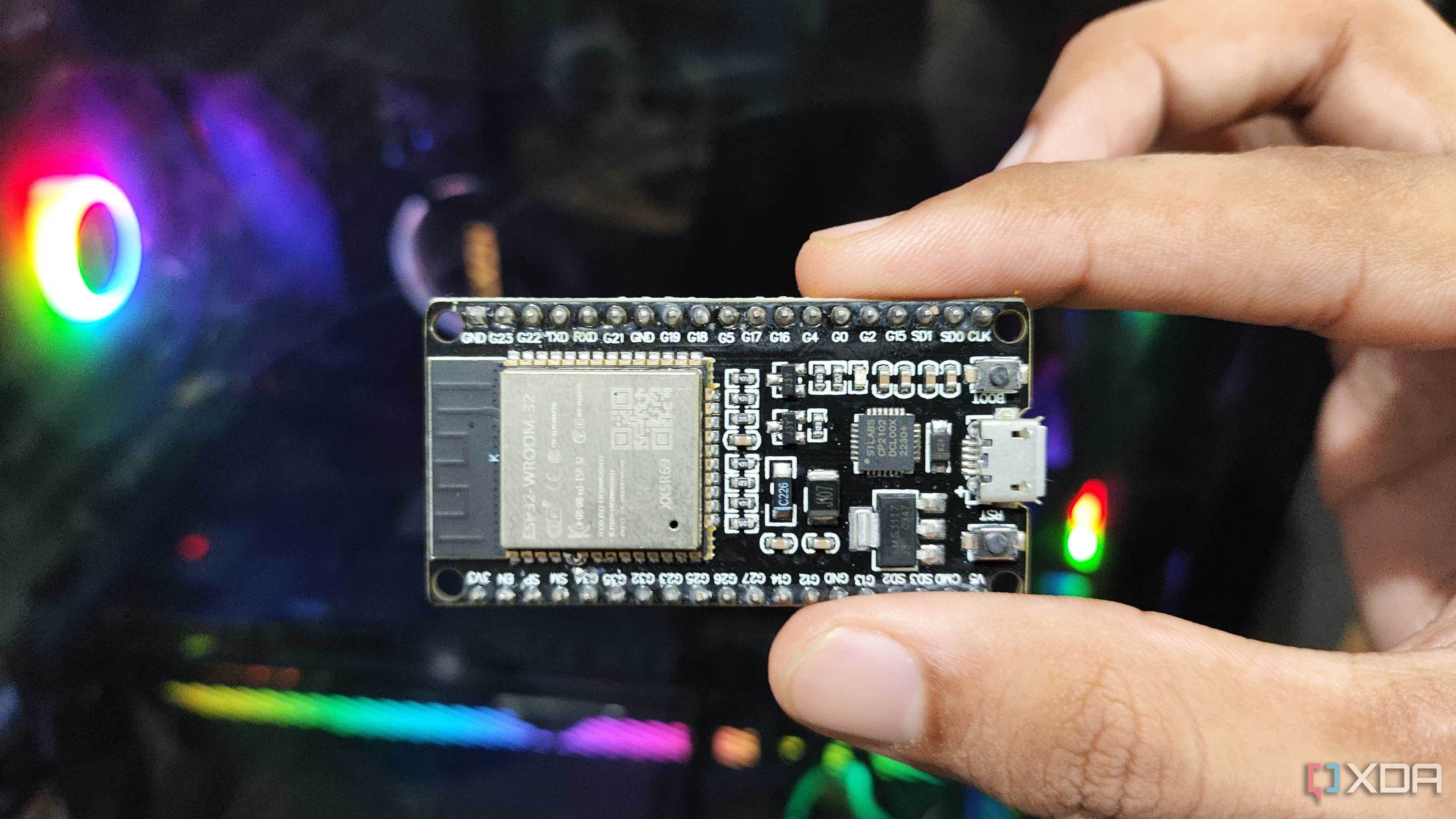 A person holding an SP32 microcontroller in front of a PC