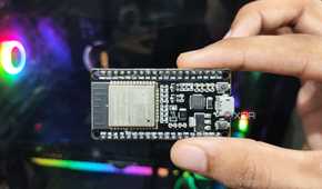 A person holding an SP32 microcontroller in front of a PC