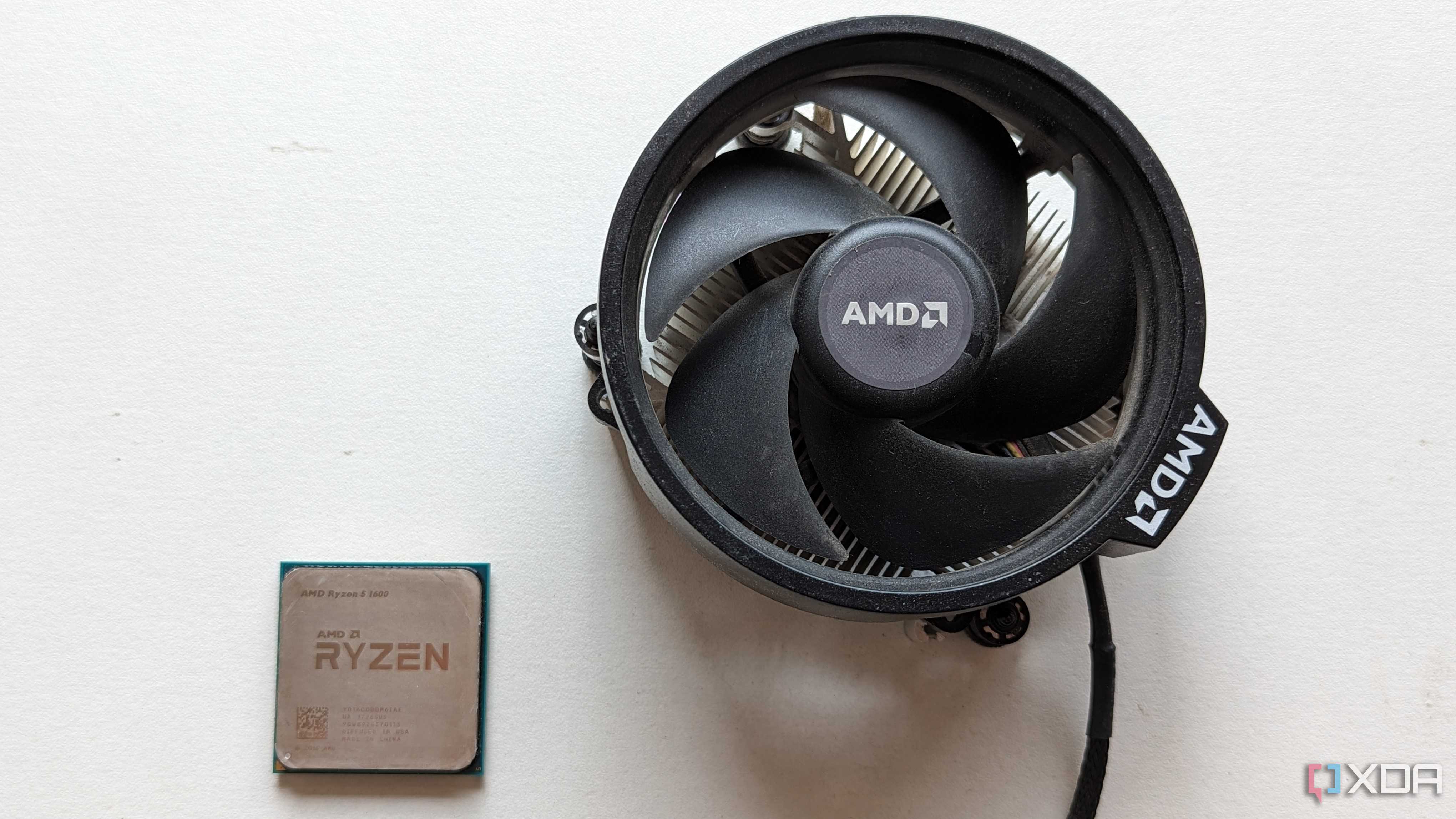 Ryzen 5 1600 CPU next to its stock cooler on a white surface