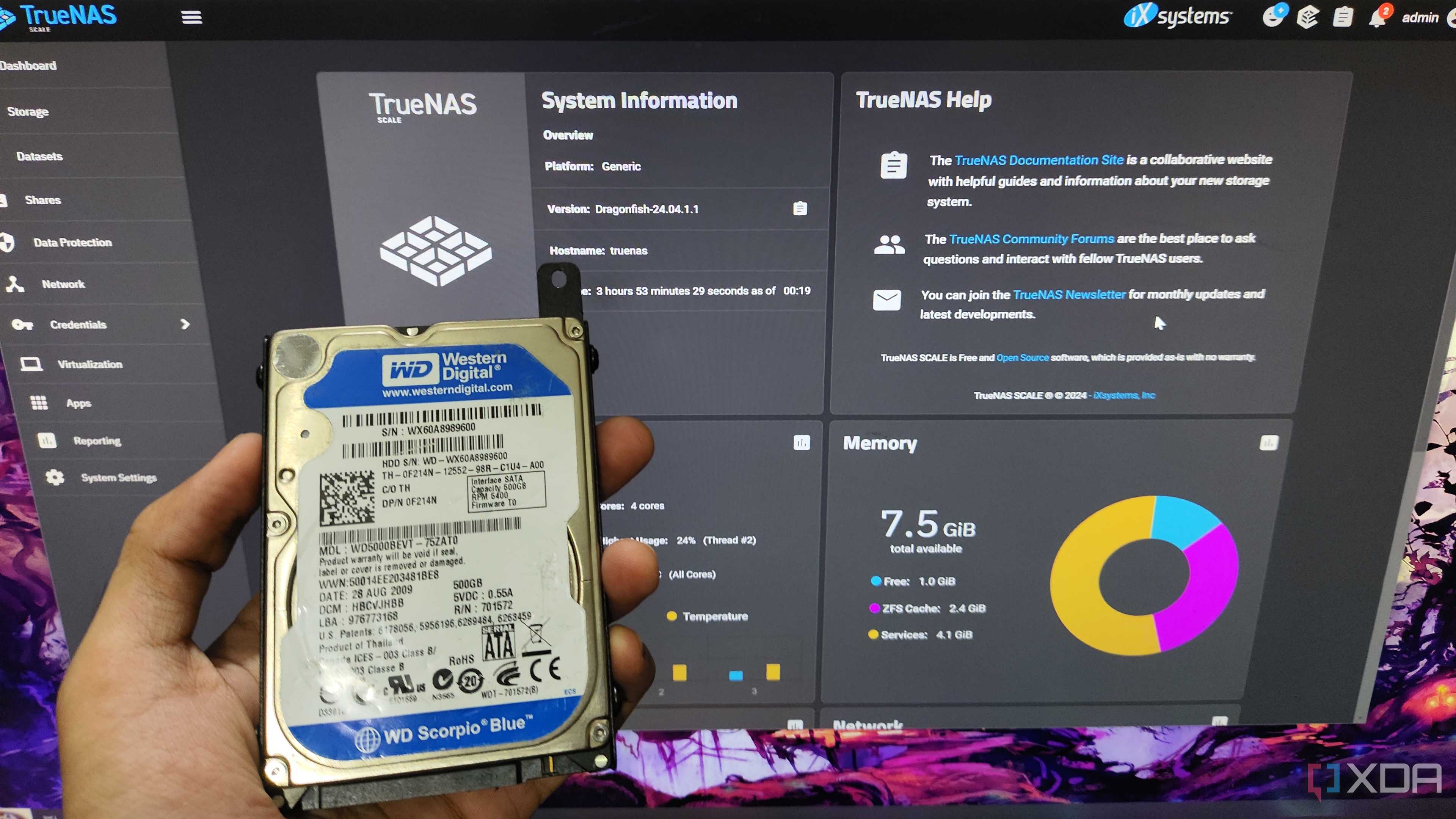 A person holding an HDD in front of a monitor displaying TrueNAS Scale web UI