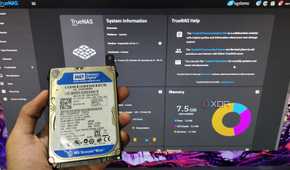 A person holding an HDD in front of a monitor displaying TrueNAS Scale web UI