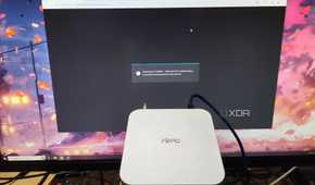 An Aiffro K100 NAS held in front of a monitor displaying the TrueNAS web UI