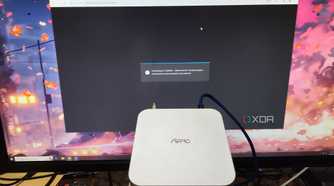 An Aiffro K100 NAS held in front of a monitor displaying the TrueNAS web UI