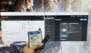 A person holding an HDD and an SSD in front of a monitor displaying the TrueNAS Scale and Unraid web UIs