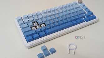 A blue-white keyboard on a white surface showing keycaps, switches, and a keycap puller