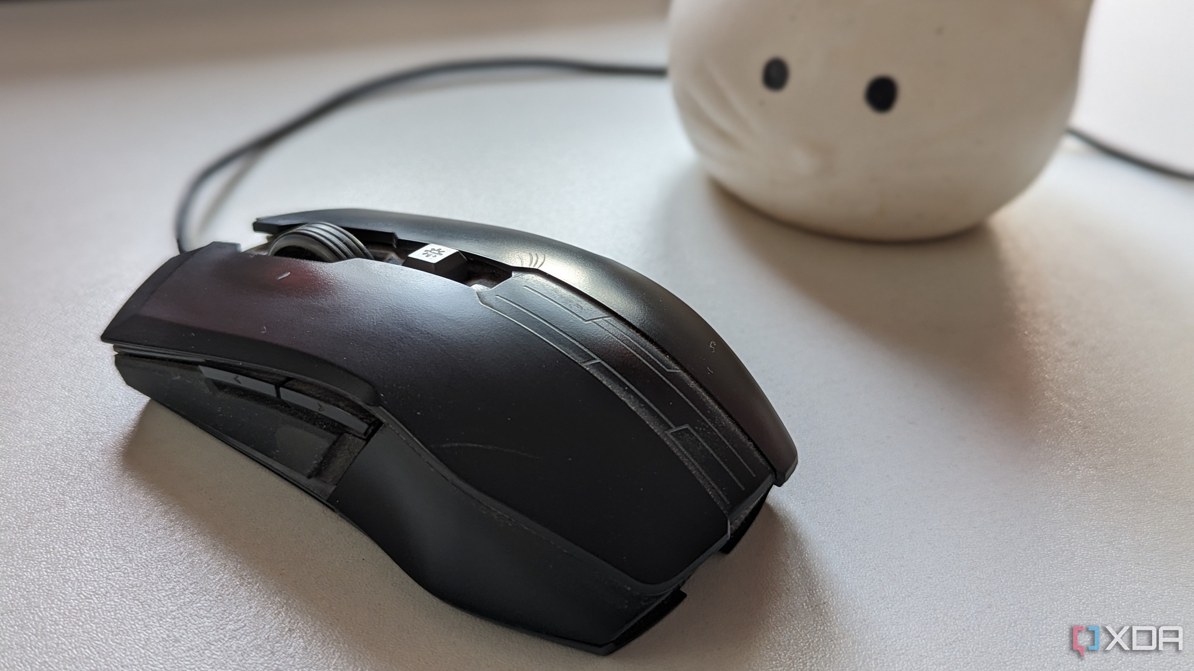 A black wired gaming mouse on a white surface next to a plant
