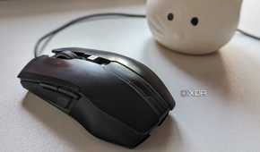 A black wired gaming mouse on a white surface next to a plant