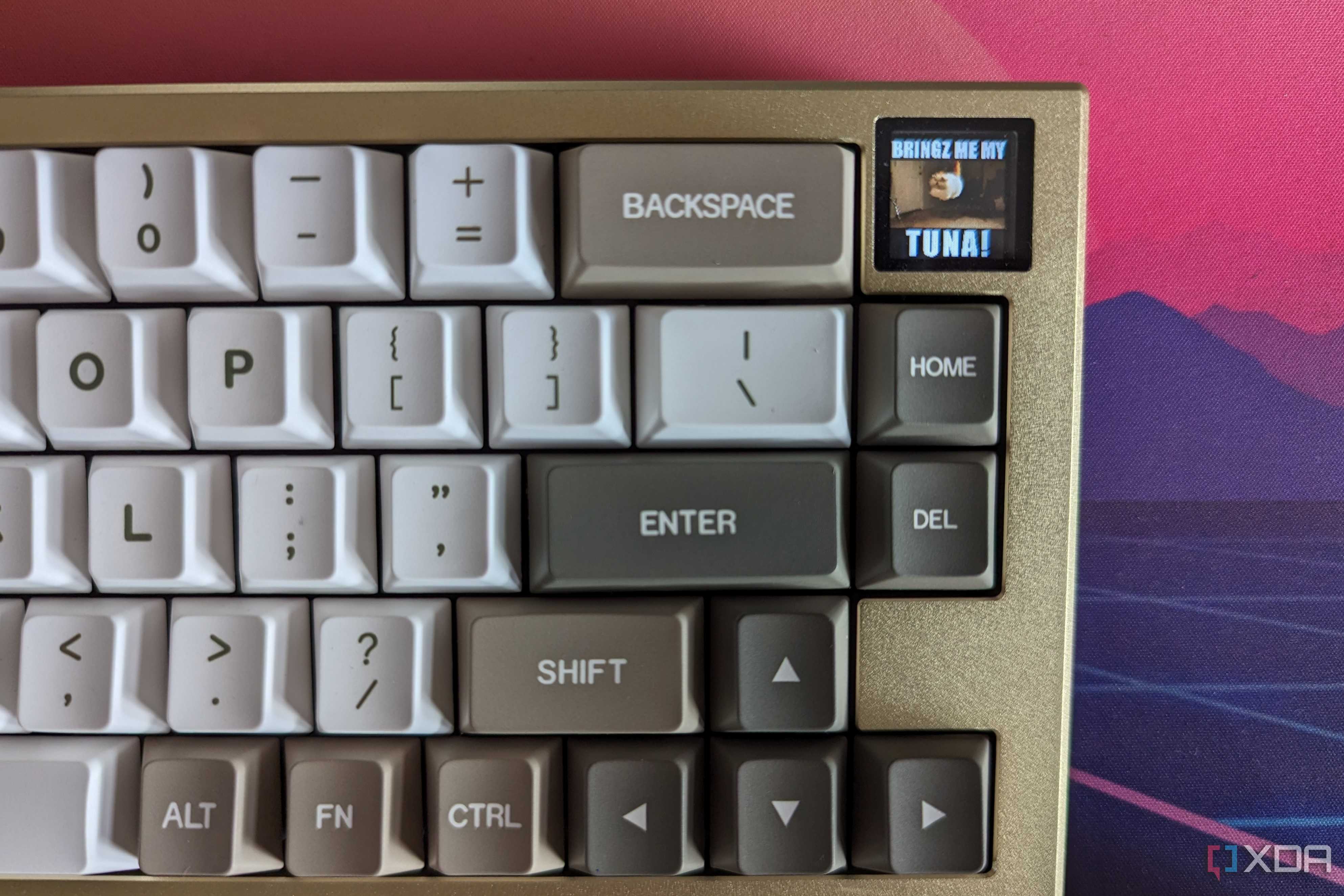 A gold and white mechanical keyboard showing a GIF on its LCD screen