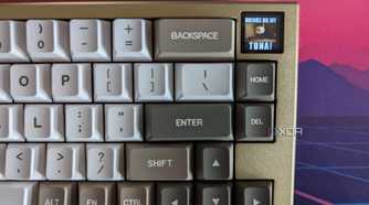 A gold and white mechanical keyboard showing a GIF on its LCD screen