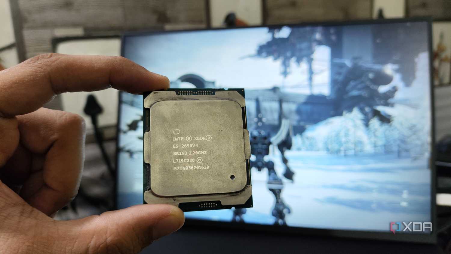 A person holding a server-grade Intel Xeon E5-2650 v4 processor in front of a monitor
