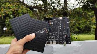 A person holding two external HDDs and an SSD in front of the Milk-V Jupiter