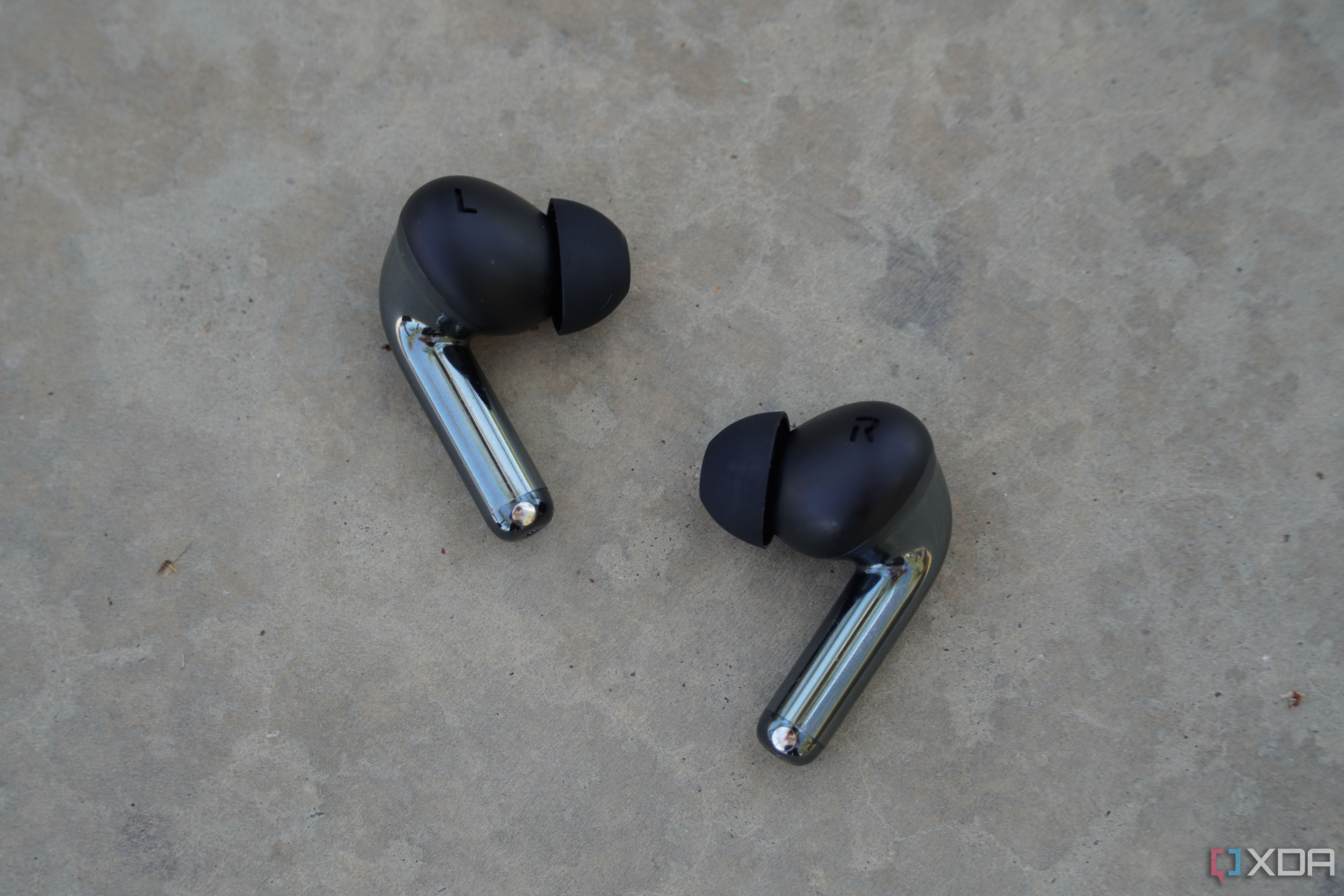 The OnePlus Buds Pro 3 earbuds on a concrete bench.