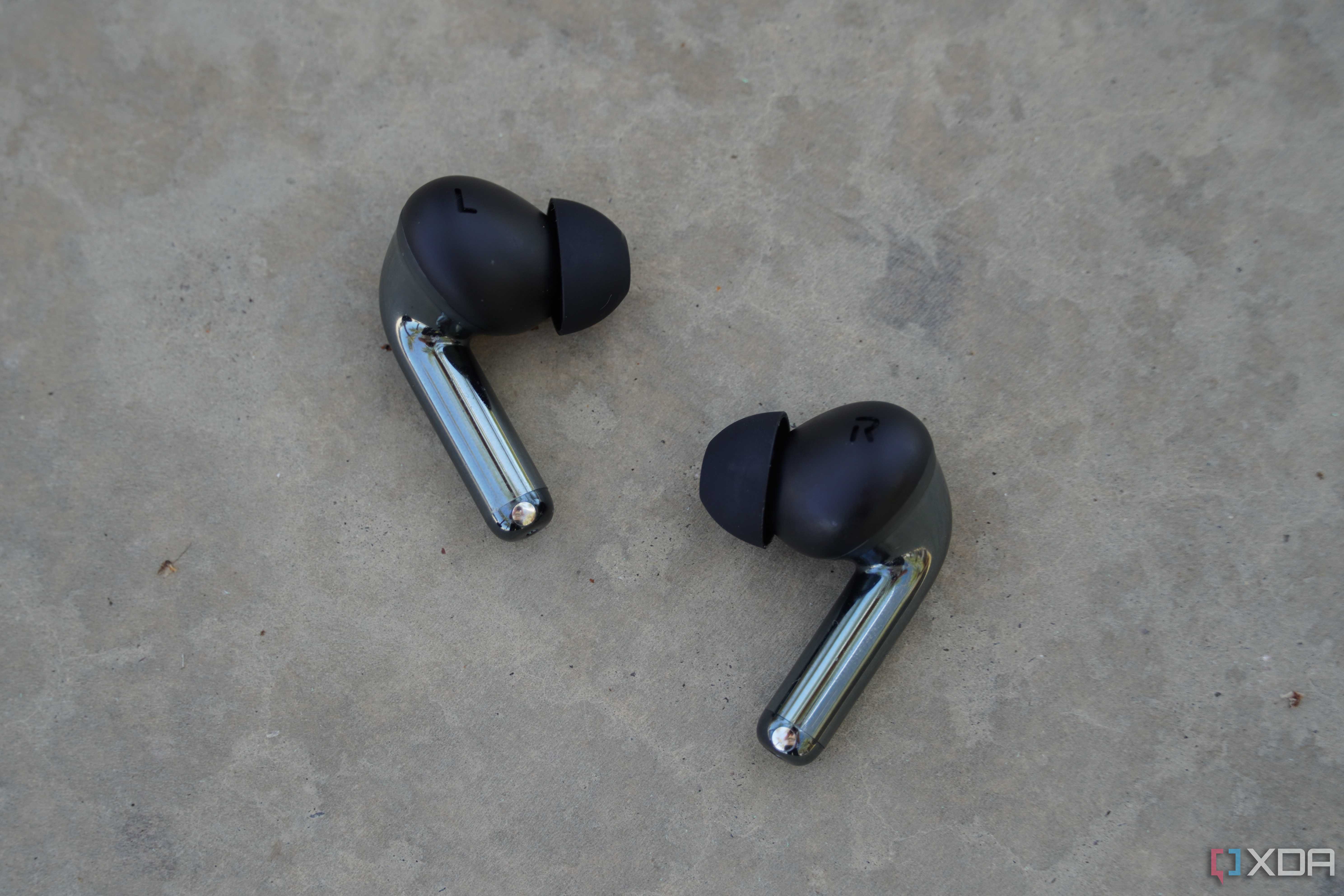 The OnePlus Buds Pro 3 earbuds on a concrete bench.