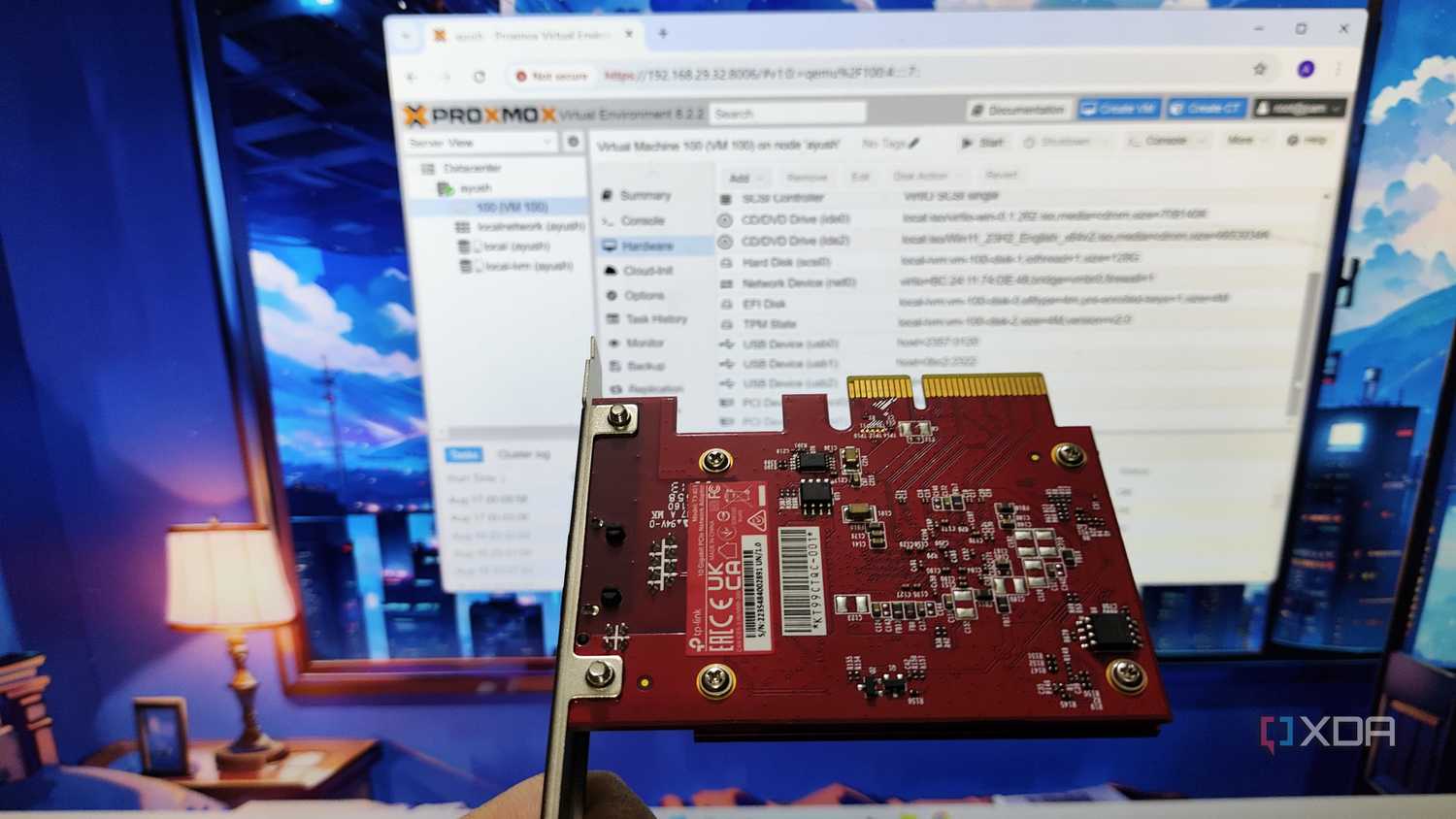 An Ethernet card held in front of a monitor running Proxmox