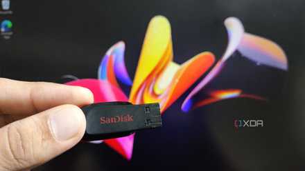 A person holding a USB drive in front of a monitor running Windows 11