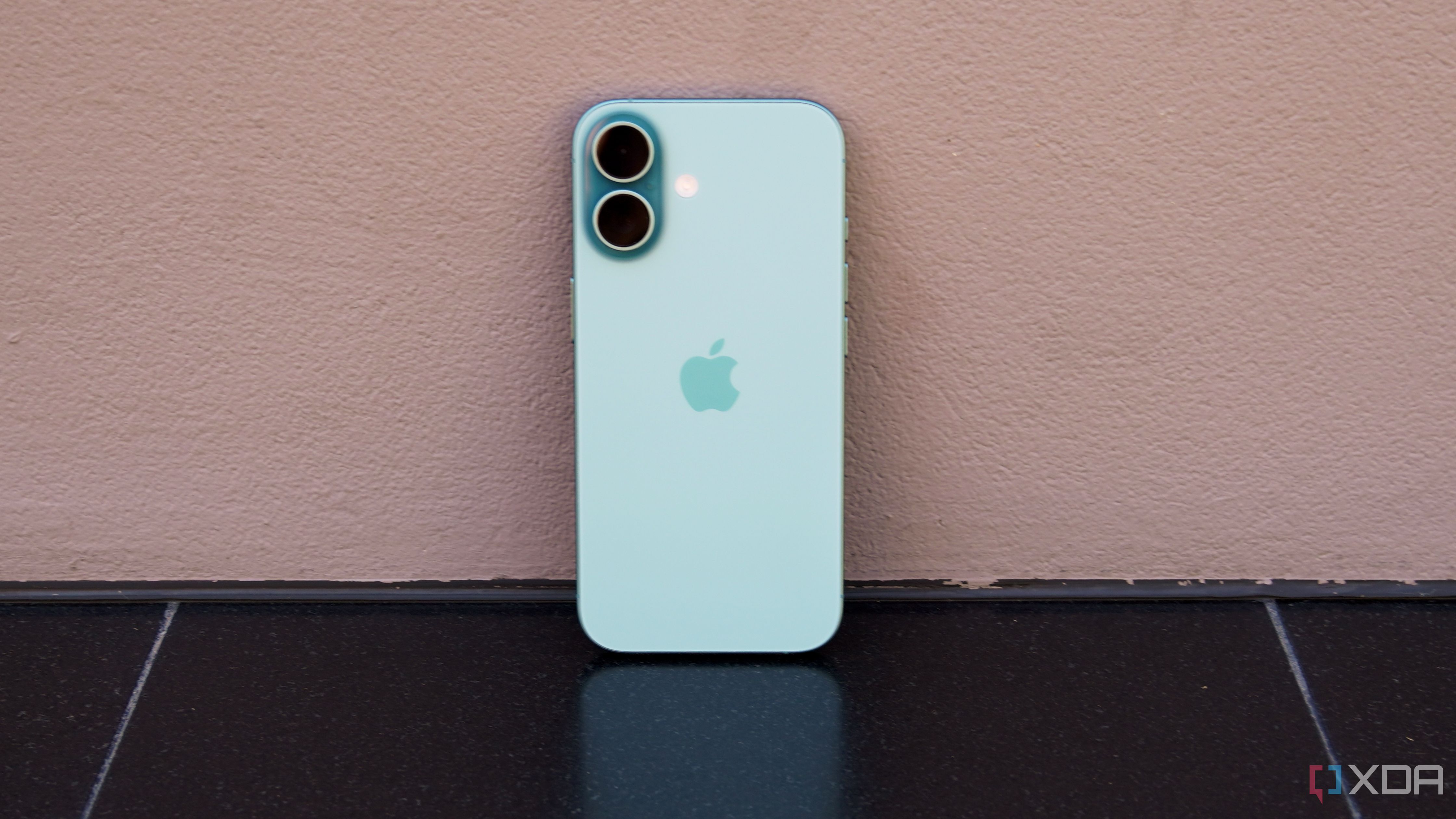 The iPhone 16 leaning against a wall in teal.