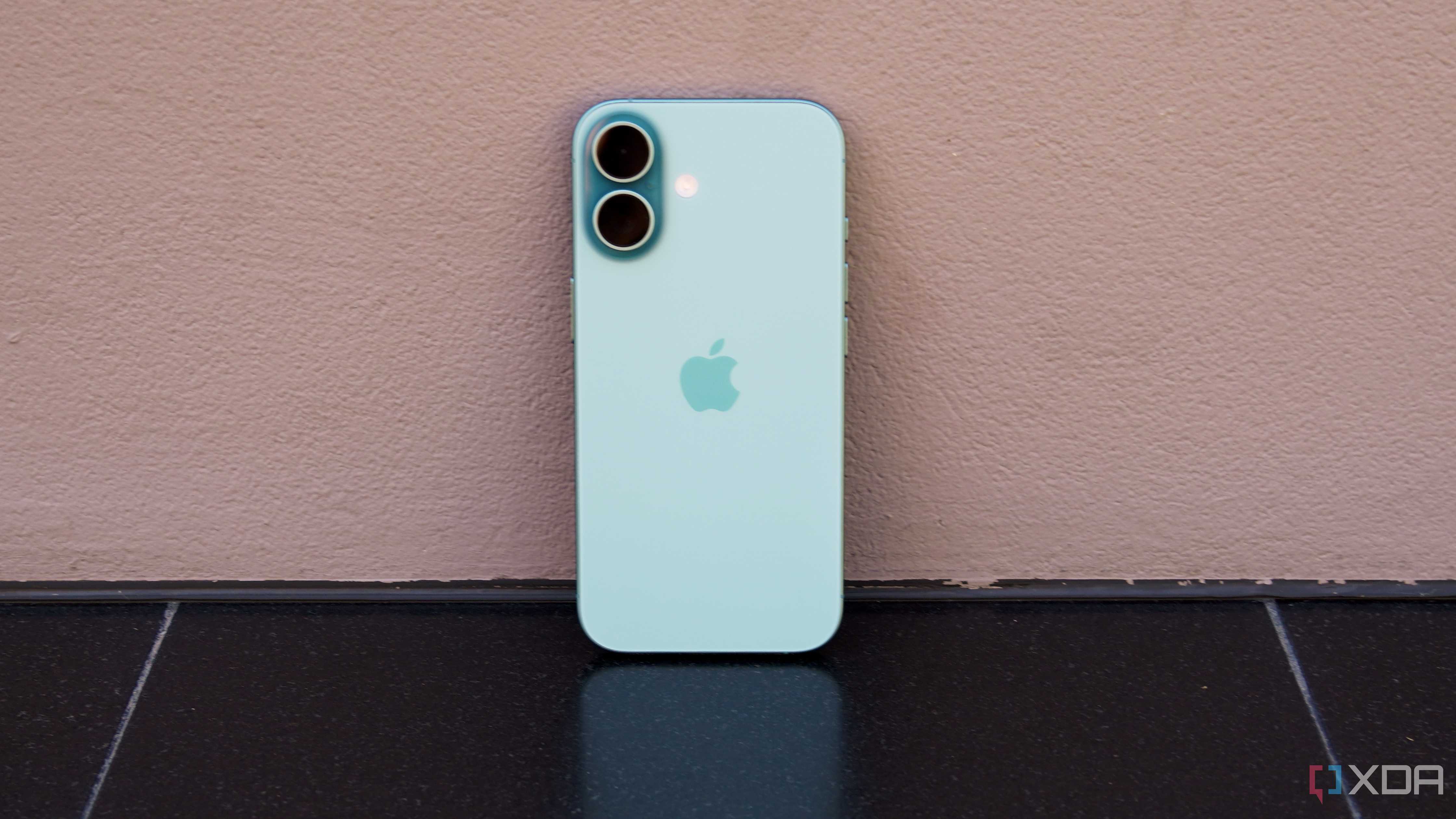 The iPhone 16 leaning against a wall in teal.