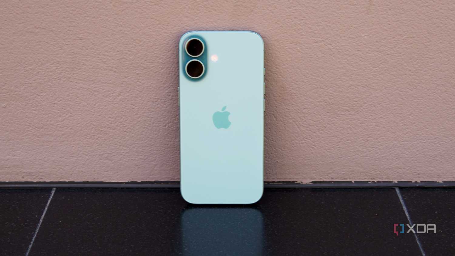 The iPhone 16 leaning against a wall in teal.