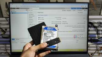 A person holding an SSD, an internal HDD and an external HDD in front of a monitor displaying the Proxmox UI