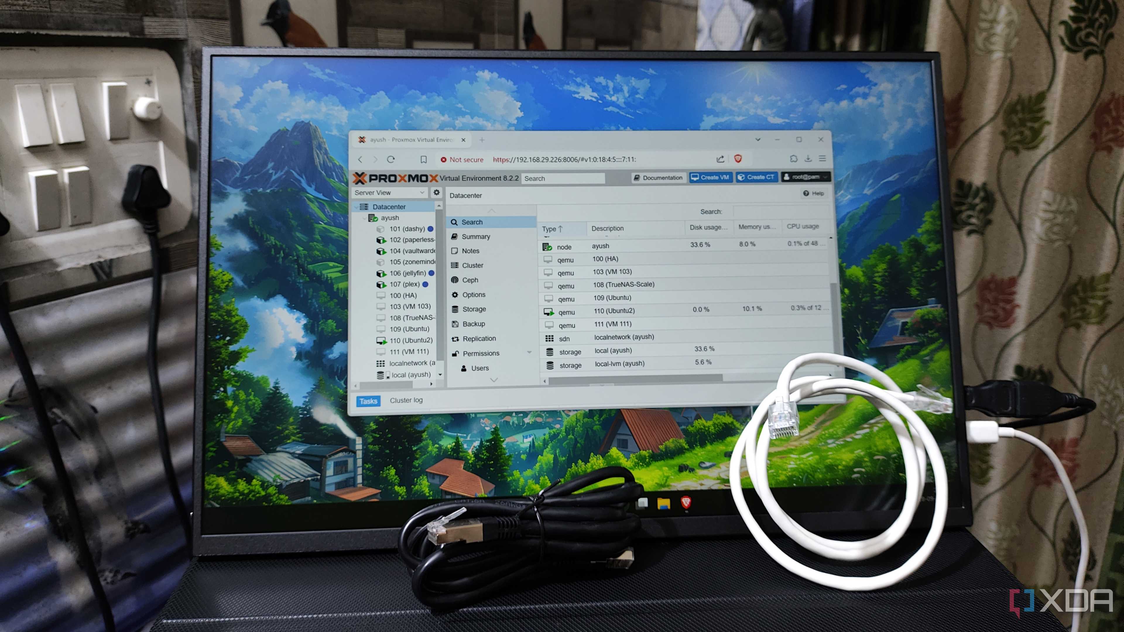 A monitor displaying the Proxmox UI, with two Ethernet cables lying in front of it