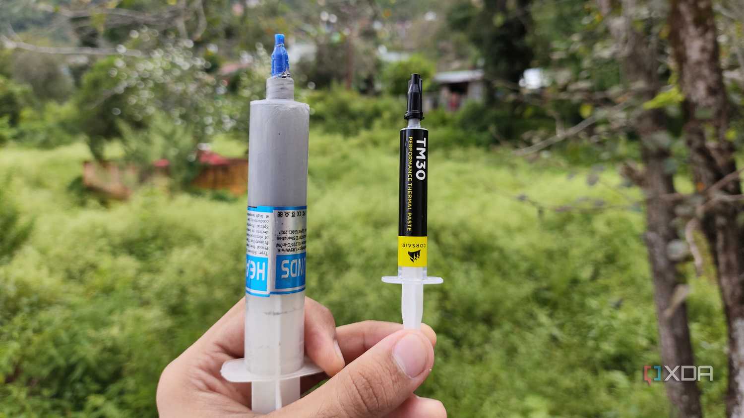 A person holding an unbranded thermal paste and a Corsair TM30