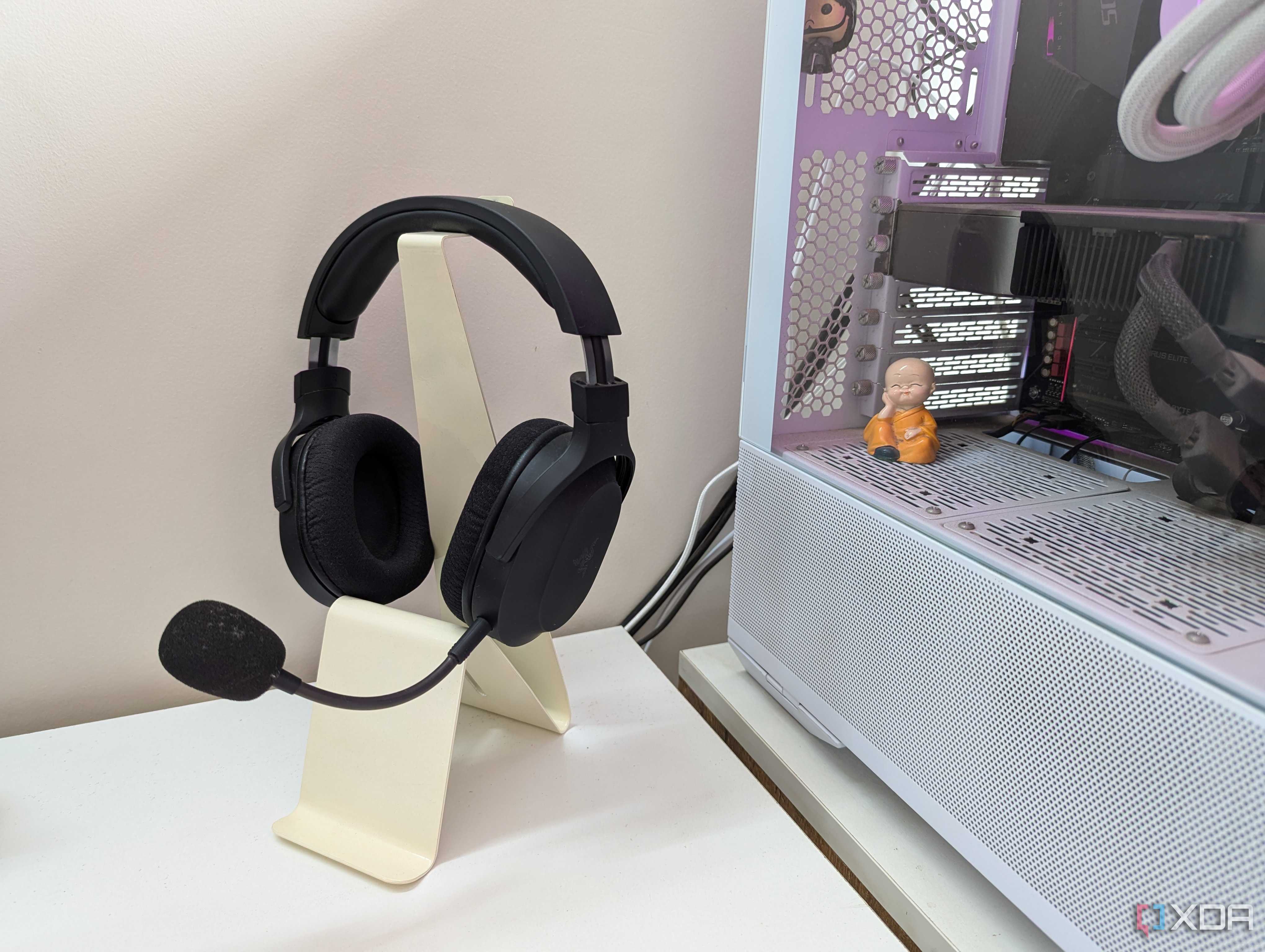 A gaming headset on a headphone stand next to a gaming PC on a white desk
