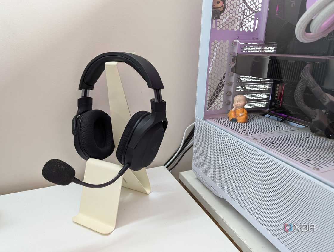 A gaming headset on a headphone stand next to a gaming PC on a white desk