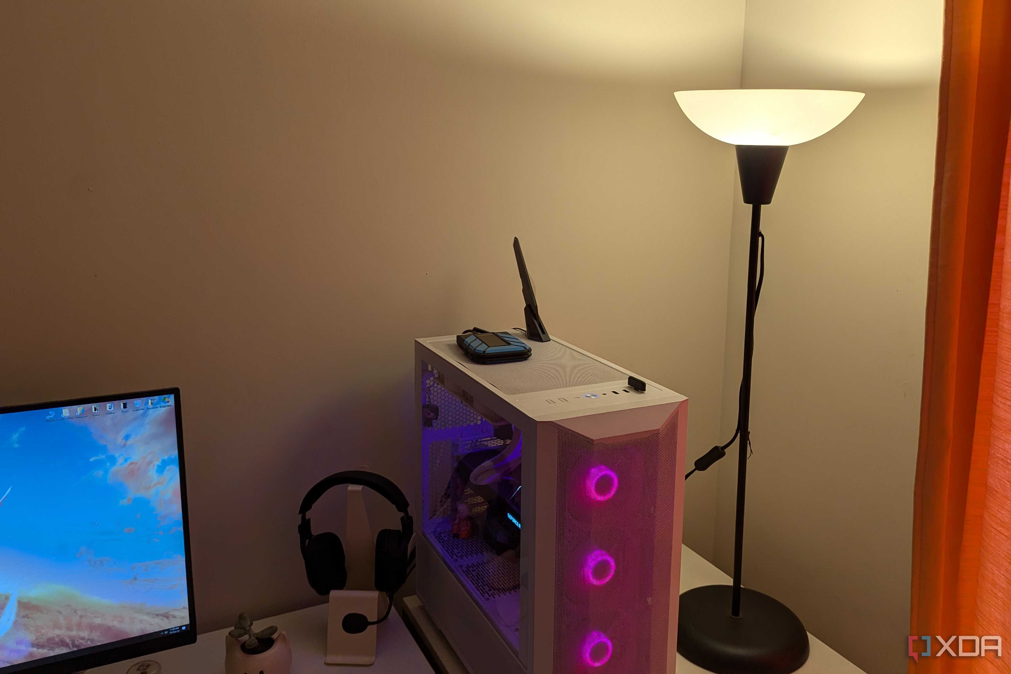 A warm lighting lamp next to a gaming PC and white desk