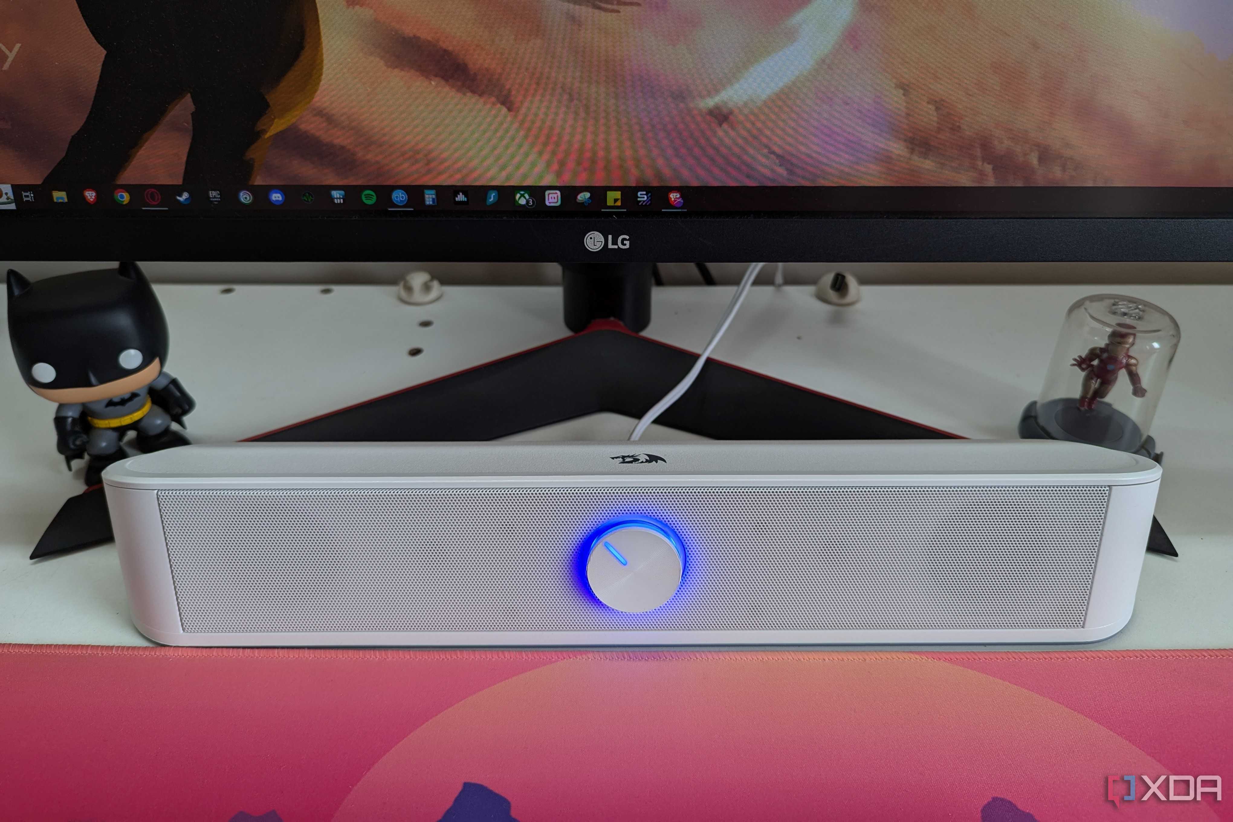 A white desktop soundbar next to a monitor and deskmat on a white desk