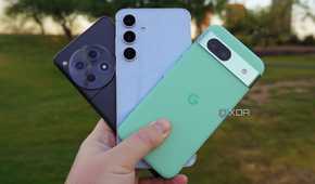The Galaxy S24 FE in blue, the OnePlus 12R in black, and the Pixel 8a in green held in a hand against a background with green grass