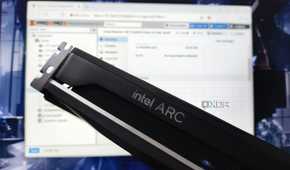 An Intel Arc GPU hovering in front of a monitor