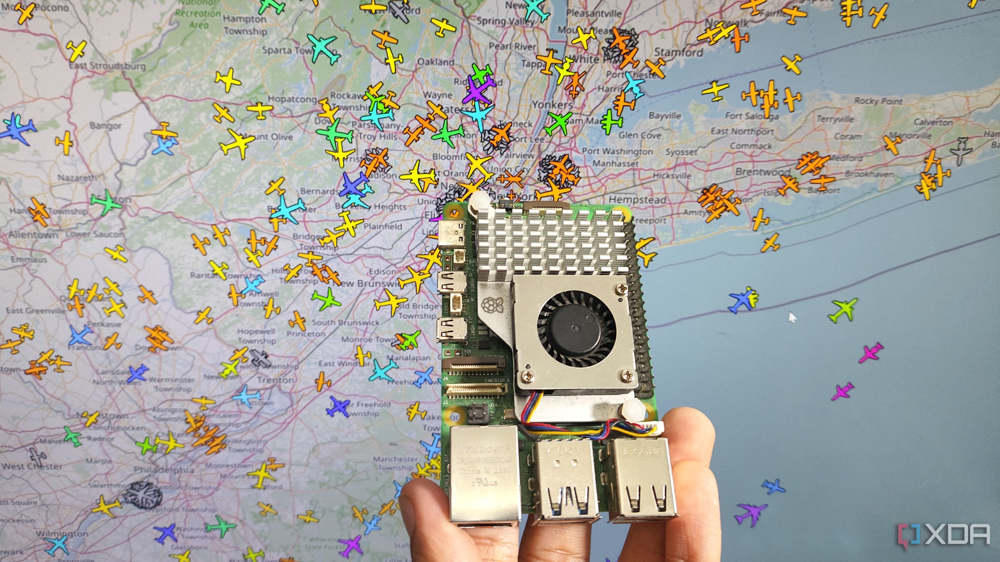 A person holding a Raspberry Pi 5 in front of an aircraft tracking system