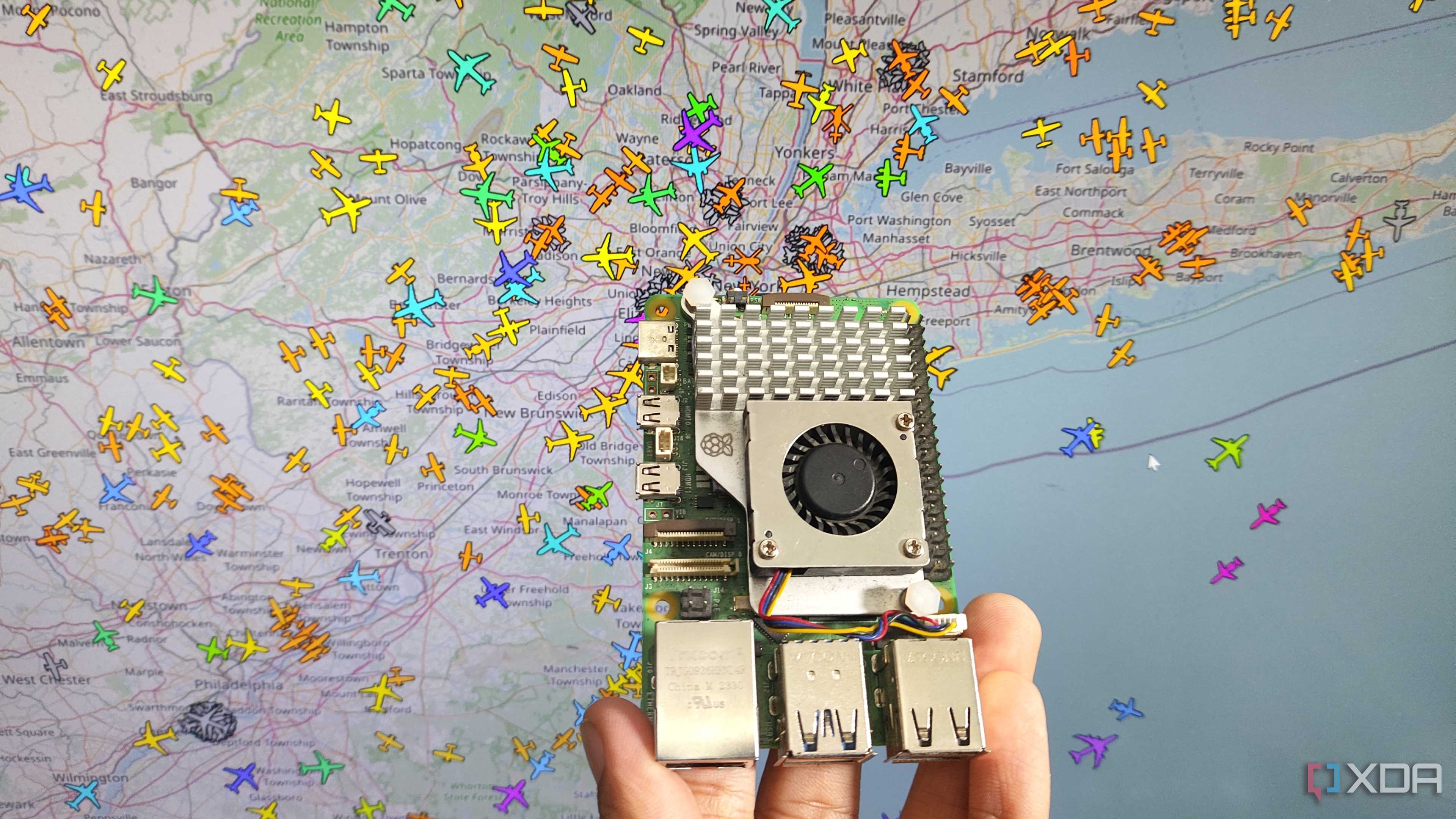 A person holding a Raspberry Pi 5 in front of an airplane tracking system